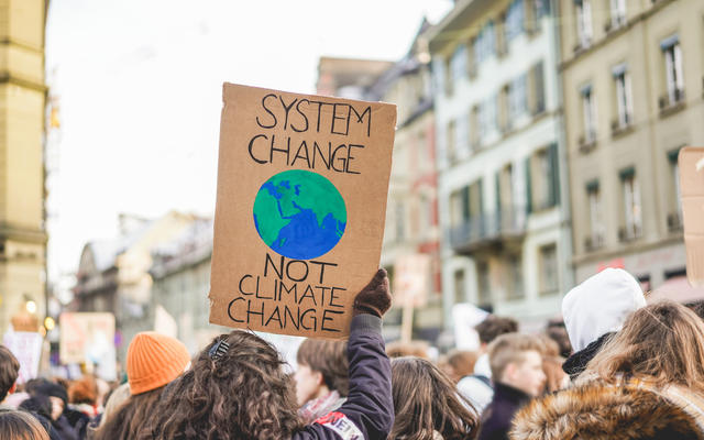 March protest placard reading "Systems Change not Climate Change" with crowd in the background